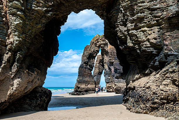 туристы под природными каменными арками соборы пляж - tide rock bay landscape стоковые фото и изображения