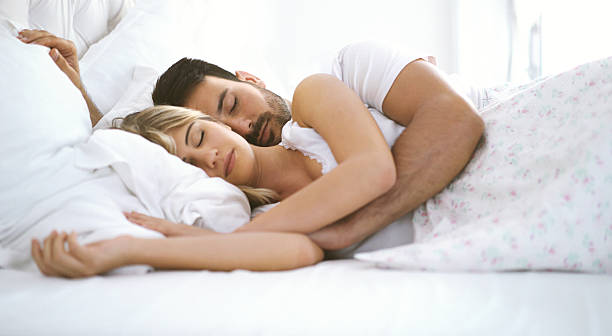 Sleeping couple. Closeup side view of mid 20's couple comfortably sleeping in bedroom. They are embraced and facing camera. double bed photos stock pictures, royalty-free photos & images