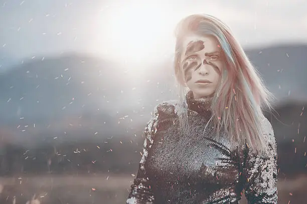 sunset shot of warrior woman with deep look staring at camera, black face paint, shiny fire sparkles in the wind.