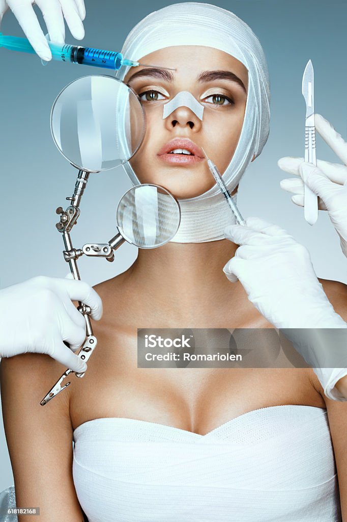 Beauty victim wrapped in medical bandages Beauty victim wrapped in medical bandages while doctors with syringes, scalpels and magnifying glass near her face. Beauty concept Plastic Surgery Stock Photo