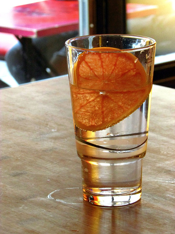 Long glass filled with water and a slice of an orange. Was served in asian restaurant in Berlin at noon time.