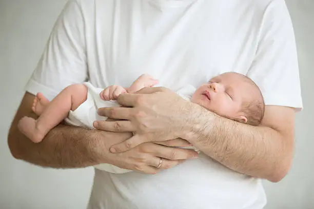 Photo of Newborn baby sleeping in mans arms