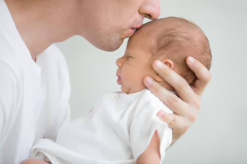 Close-up portrait of happy young father hugging and kissing his sweet adorable newborn child. Indoors shot, concept image