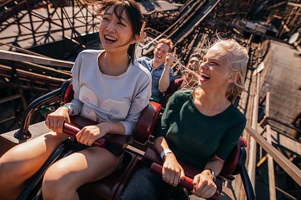 smiling young people riding a roller coaster - lunapark treni stok fotoğraflar ve resimler