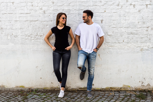 Young couple chatting while leaning comfortably against a brick wall looking at each other and smiling