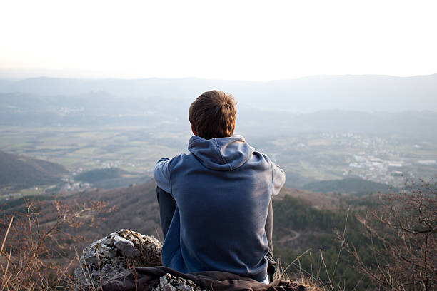 Young man looking at the view, copyspace Young man looking at the view and sitting on a rock. Copyspace above the horizon. view into land stock pictures, royalty-free photos & images