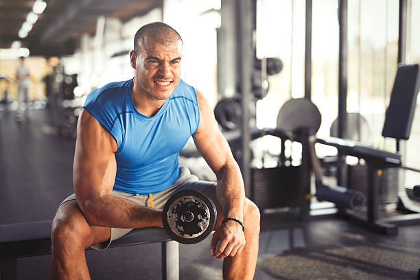 Image of a young muscular man doing exercises with dumbbells at the gym. Front view.