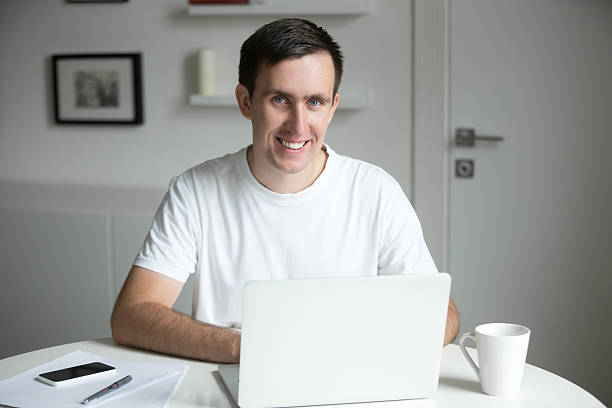 istock Handsome smiling man at the white desk working with laptop 618200086