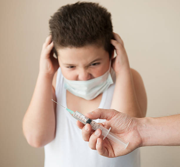 istock hand with syringe in front of   scared boy in mask 618200340