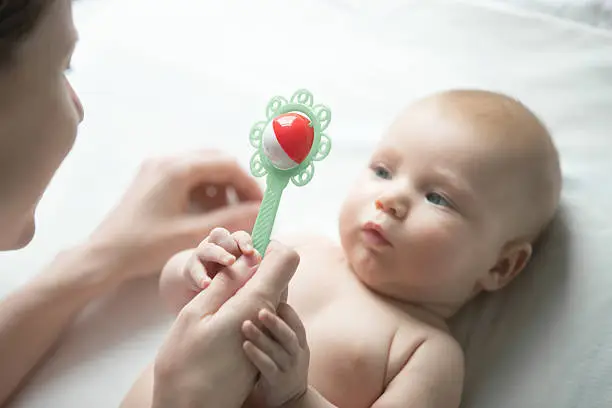 Portrait of a cute newborn lying, looking at mother's hand with a rattle. Family concept photo, lifestyle, view above, focus on a toy