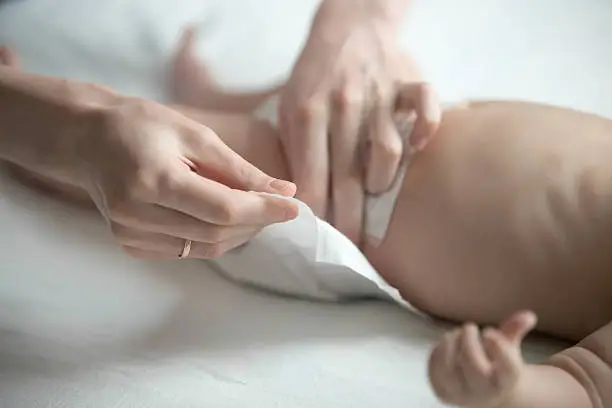 Female hands fixing a diaper on a newborn lying. Family concept photo, lifestyle, close up
