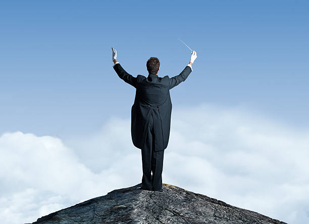 musikalischer dirigent auf dem gipfel des berges mit erhobenen armen - dirigent stock-fotos und bilder