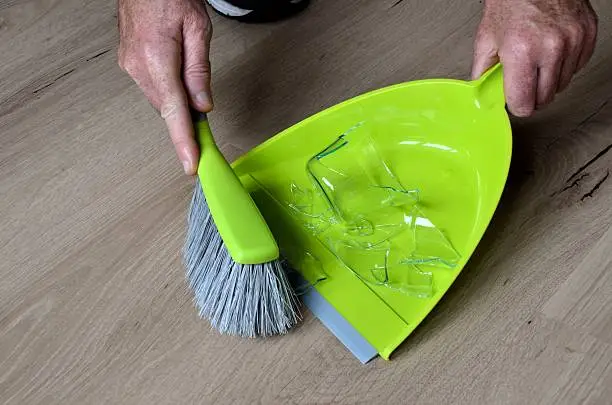 Clean up broken water glass with broom and dustpan
