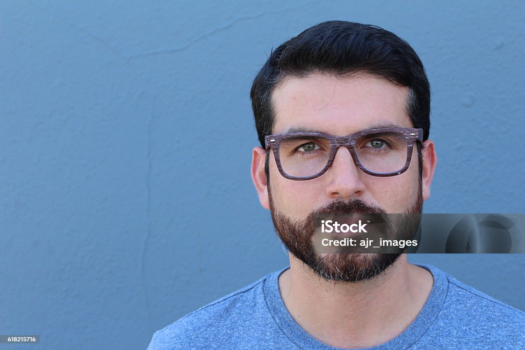 Gorgeous bearded brunette guy wearing glasses Gorgeous guy wearing glasses leaning on blue wall with copy space. 30-39 Years Stock Photo