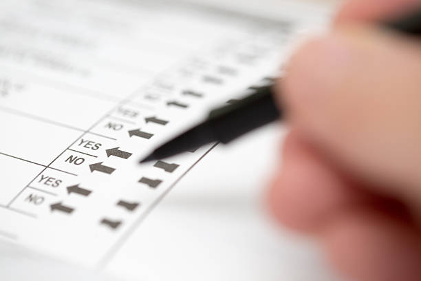 Selective focus on Yes or No options on an election ballot with a blurred hand holding a marker to cast a vote
