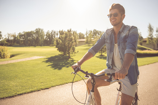 Handsome man in sun glasses is smiling while cycling in the park