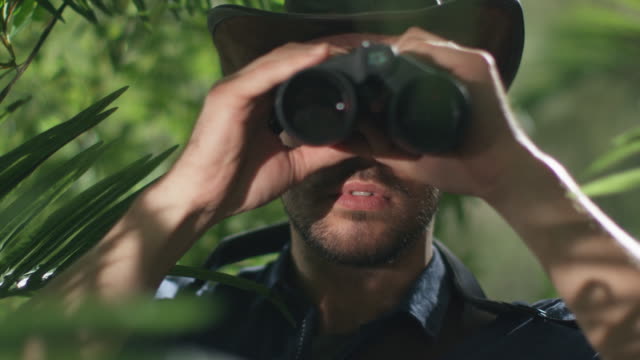 Adventurer in Hat Walking through Jungle Forest And Looking through Binoculars