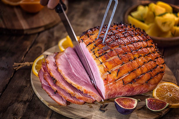 carving glazed holiday ham with cloves - geroosterd fotos stockfoto's en -beelden