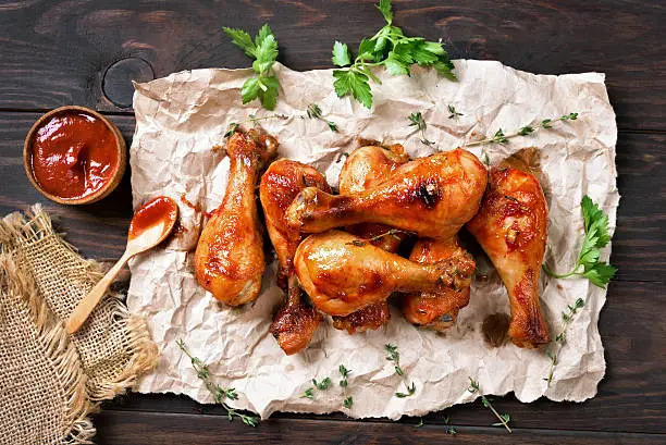 Grilled chicken drumstick on paper over wooden background, top view