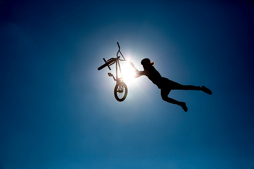 Sofia, Bulgaria - September 24, 2016: An extreme rider is making a free style jump from a ramp. The young boy with his bicycle is seen as a silhouette in front of the sun.  