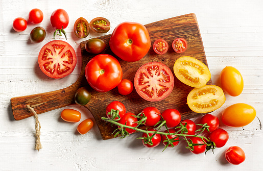 various colorful tomatoes on wooden cutting board, top view