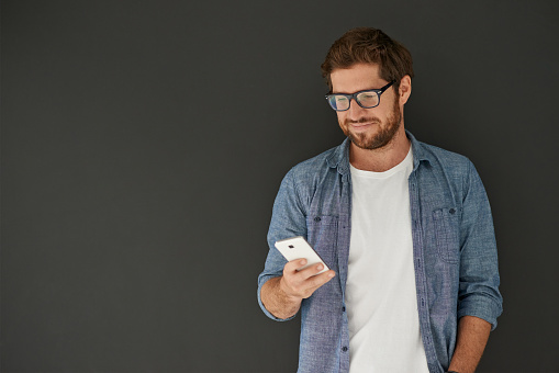 Studio shot of a young man reading a text message against a grey background