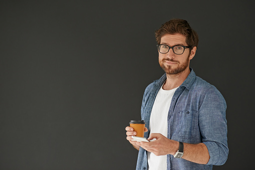 Studio portrait of a young man drinking coffee and sending a text against a grey background
