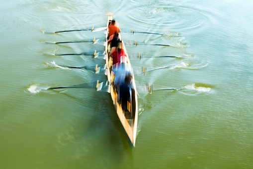 Teamwork, motion blurred rowers in a rowing boat training on a river, elevated view