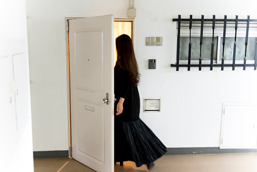 The lady who opens a door in the old apartment in Tokyo and enters a room.