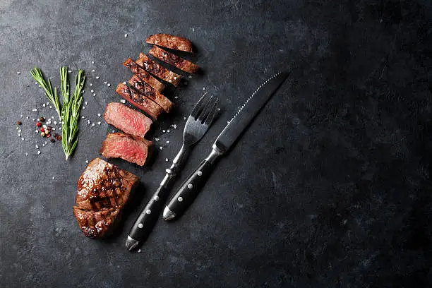 Grilled sliced beef steak on stone table. Top view with copy space