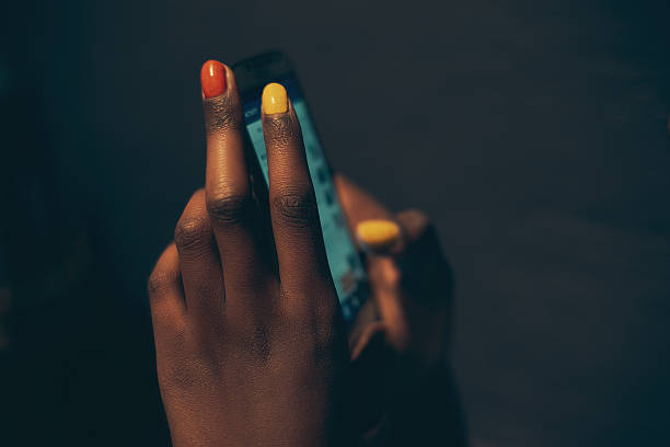 Close-up of female hands with nail art holding and using smartphone, dark blurred background