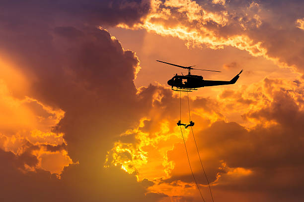    silhouette soldiers in action rappelling climb down from helicopter with military mission counter terrorism assault training on sunset background 