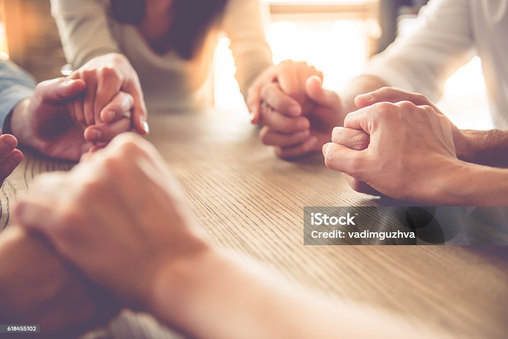 Business people working Cropped image of beautiful business team holding hands and praying while sitting in office Praying Stock Photo
