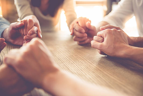 Business people working Cropped image of beautiful business team holding hands and praying while sitting in office praying photos stock pictures, royalty-free photos & images