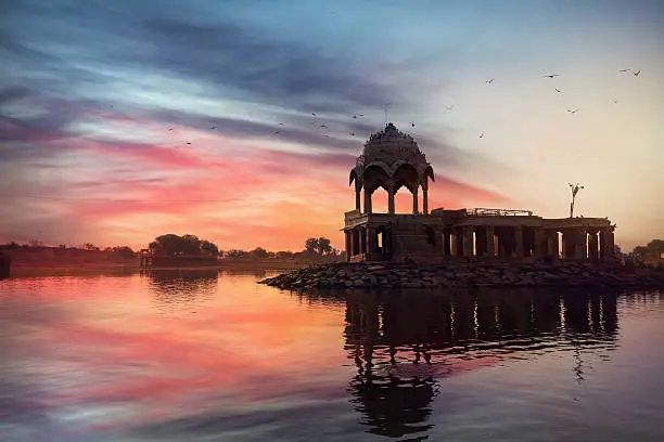 Silhouette of Temple on the Gadi Sagar lake at pink vibrant sunset sky in Jaisalmer, Rajasthan, India