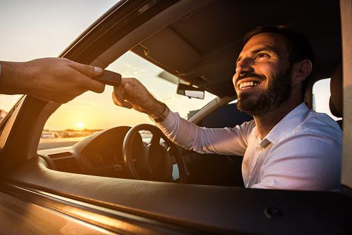 Happy businessman taking the car keys from unrecognizable person at sunset.