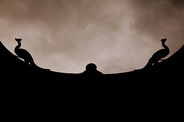 Silhouette of temple roof with two phoenix against sky. 