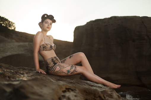 Pinup model in the swimsuit sitting on the rock with make up and hairstyle. Beautiful and sexy woman on the beach, vacation time on the sea. 