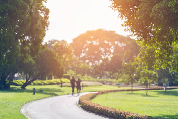 Blurry focus scene of couple walking on the path inside public park with soft orange sunlight in morning.
