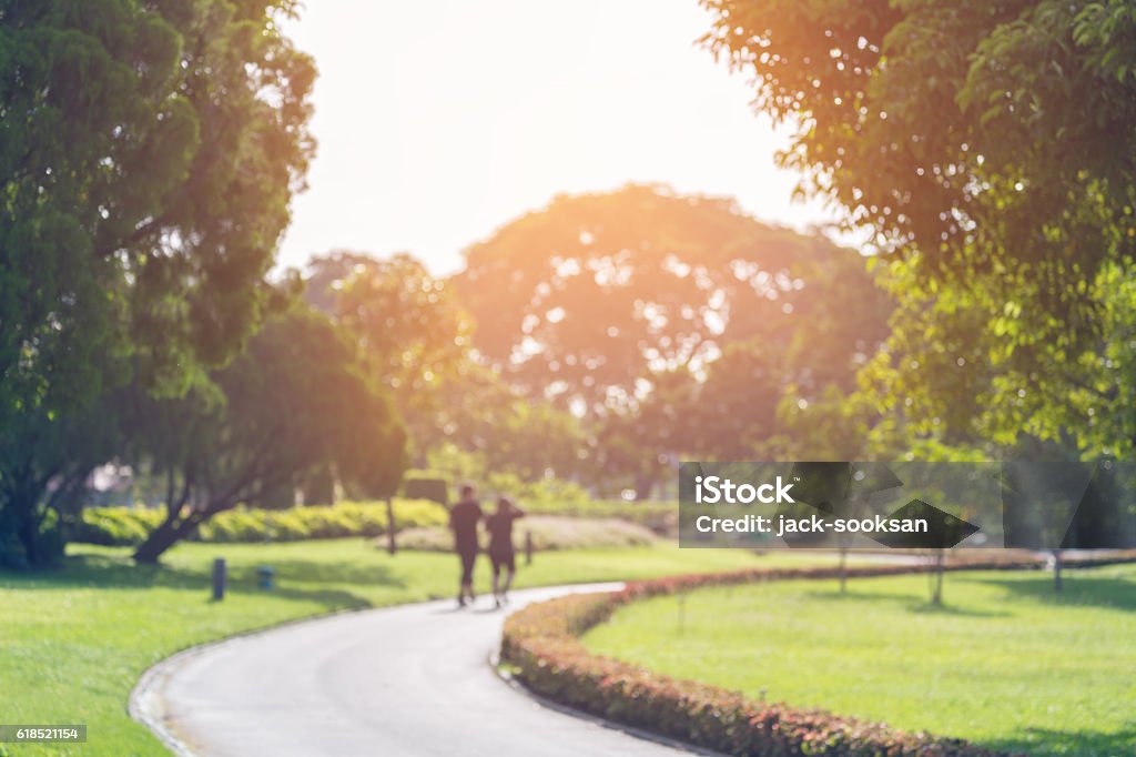 Blurry focus scene of people in public park Blurry focus scene of couple walking on the path inside public park with soft orange sunlight in morning. Public Park Stock Photo