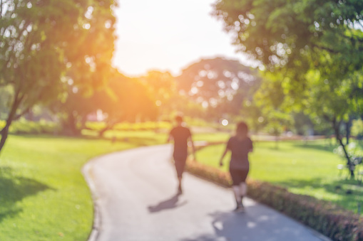 Blurry focus scene of couple walking on the path inside public park with soft orange sunlight in morning.