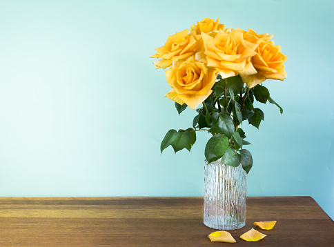Yellow roses in a glass vase on wood table