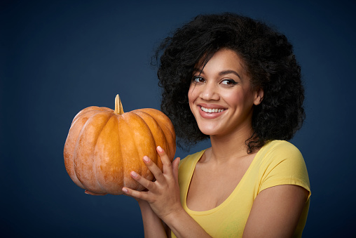 Smiling joyful woman holding ripe pumpkin isolated over blue background