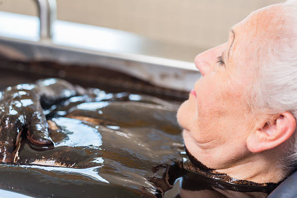 femme âgée profitant d’une thérapie alternative au bain de boue - bain de boue thérapie du bien être photos et images de collection