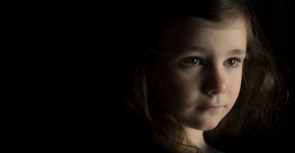 Portrait of young girl in studio on black background with copy space