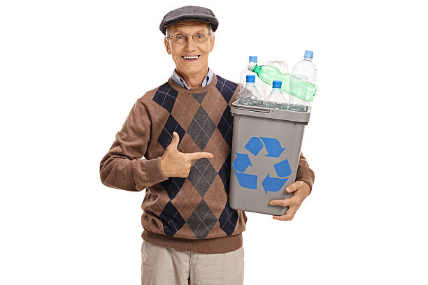 Cheerful elderly man holding a recycling bin full of plastic bottles and pointing isolated on white background