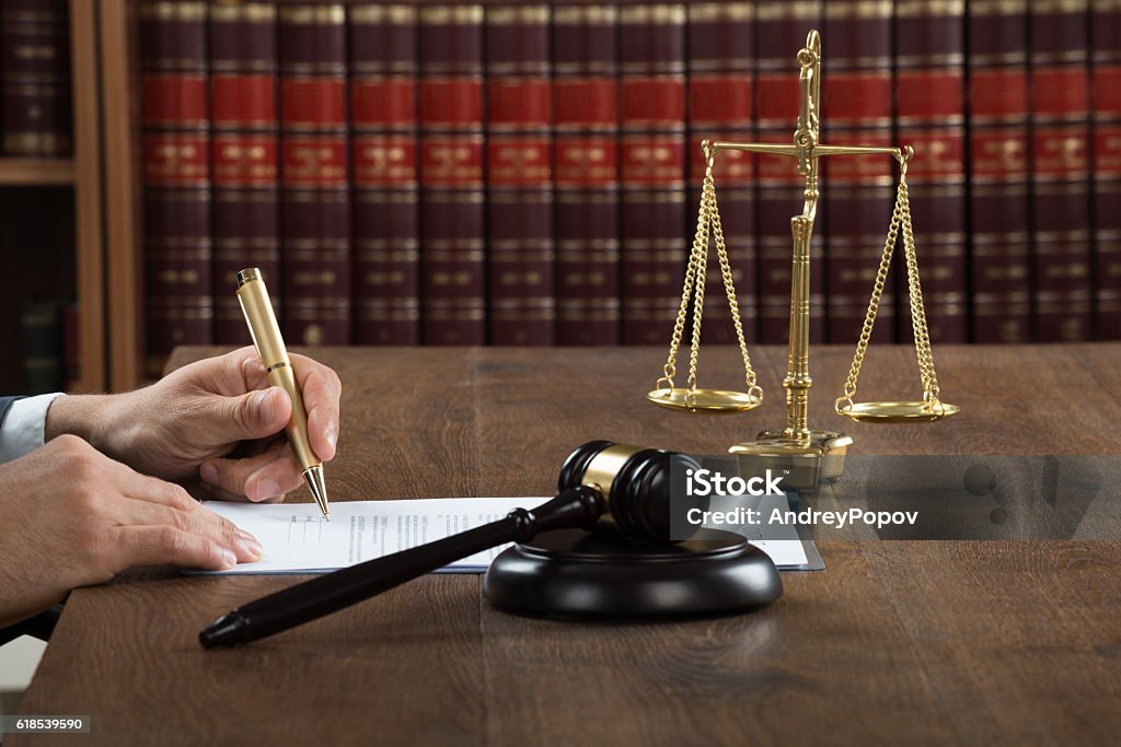 Judge Writing On Legal Documents At Desk Cropped image of male judge writing on legal documents at desk in courtroom Adult Stock Photo