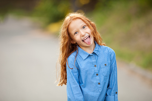 Portrait of attractive caucasian little child girl with blond curly hair and cute smile. Happy smiling child looking at camera - close-up, outdoors.