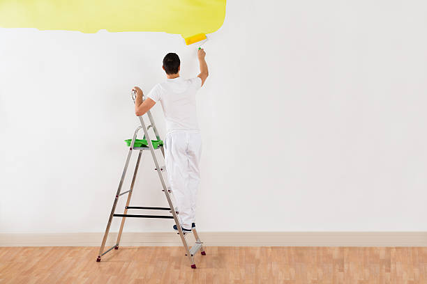 istock Man Painting Wall With Yellow Paint Roller 618540714