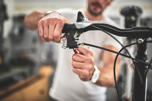 Close up shot on the hands of a mechanic inside bicycle store while repairing the hand brake on mountain bike.